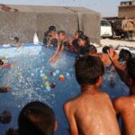 Displaced Syrian children play in a mobile swimming pool set up by the  Smile Younited charity organisation, during the sweltering summer heat in the Kafr Naseh camp, in the rebel-held part of Aleppo province on July 27, 2024. - The pools at the camp for displaced people provided rare entertainment to young boys and girls whose lives have been scarred by war and poverty. (Photo by AAREF WATAD / AFP)